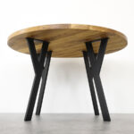 Drvena okrugla ploča na četiri crne metalne nogice visine 71 cm za noge za stolove i stoliće Vicco pod kutom na podlozi od sivih pločica.