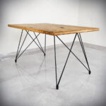 Drvena kvadratna ploča na dvije noge za stol Urban, visine 74 cm na podlozi od sivih pločica.